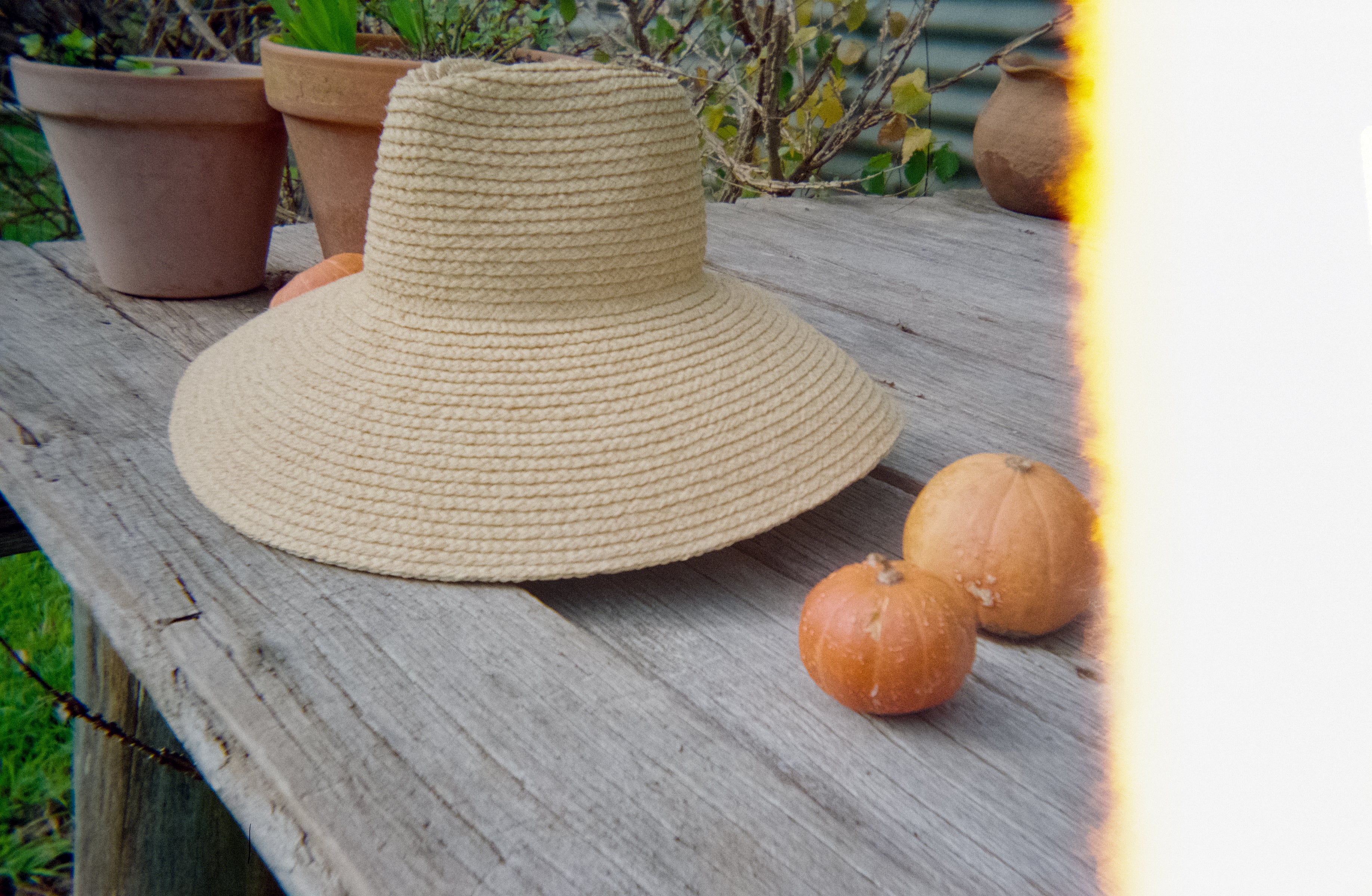 Beige sun hat on a wooden surface with pumpkins and potted plants in the background